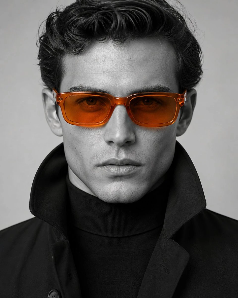 A close-up portrait of a man in orange sunglasses and a black turtleneck against a muted background.