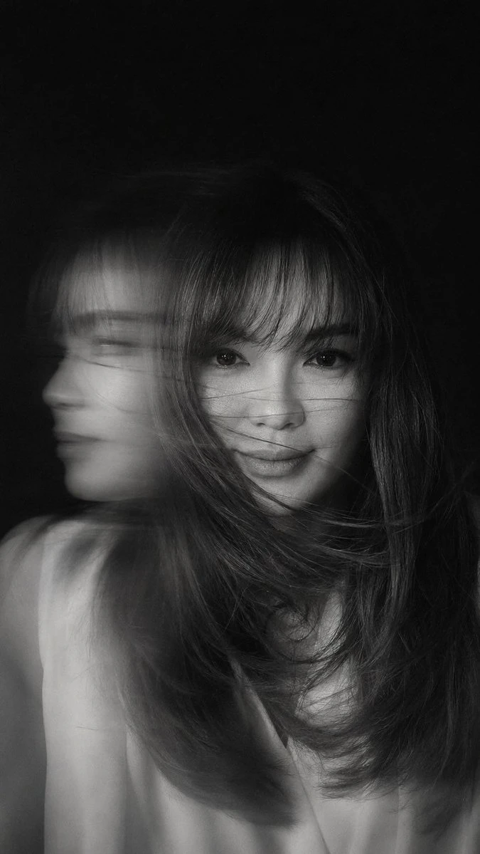 A hyper-realistic black-and-white portrait captures a woman in mid-motion, her face partially obscured by flowing hair and dynamic light streaks