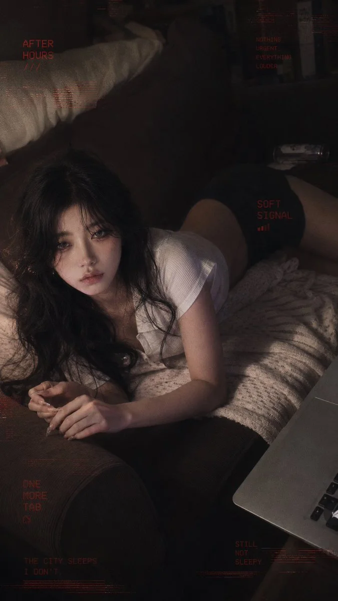 A person with long, wavy black hair lies on a couch, gazing thoughtfully with a soft expression, surrounded by a cozy atmosphere.