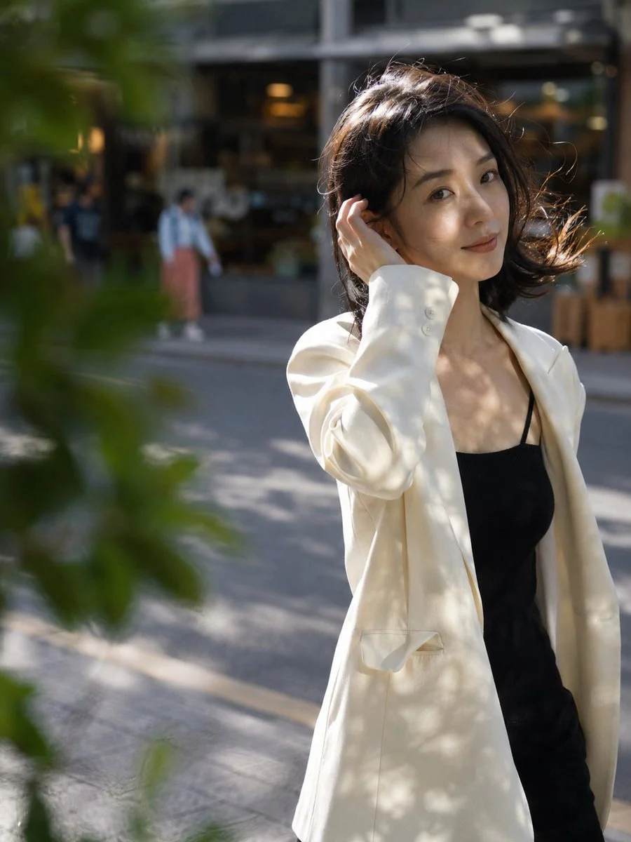 Chinese woman in an oversized blazer walking along a tree-lined city street