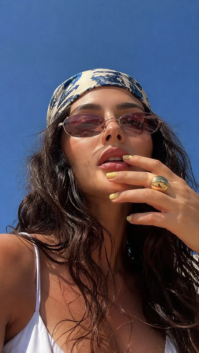 A low-angle summer macro selfie of a woman in sunlight, with bright outdoor color, close facial detail, and relaxed framing