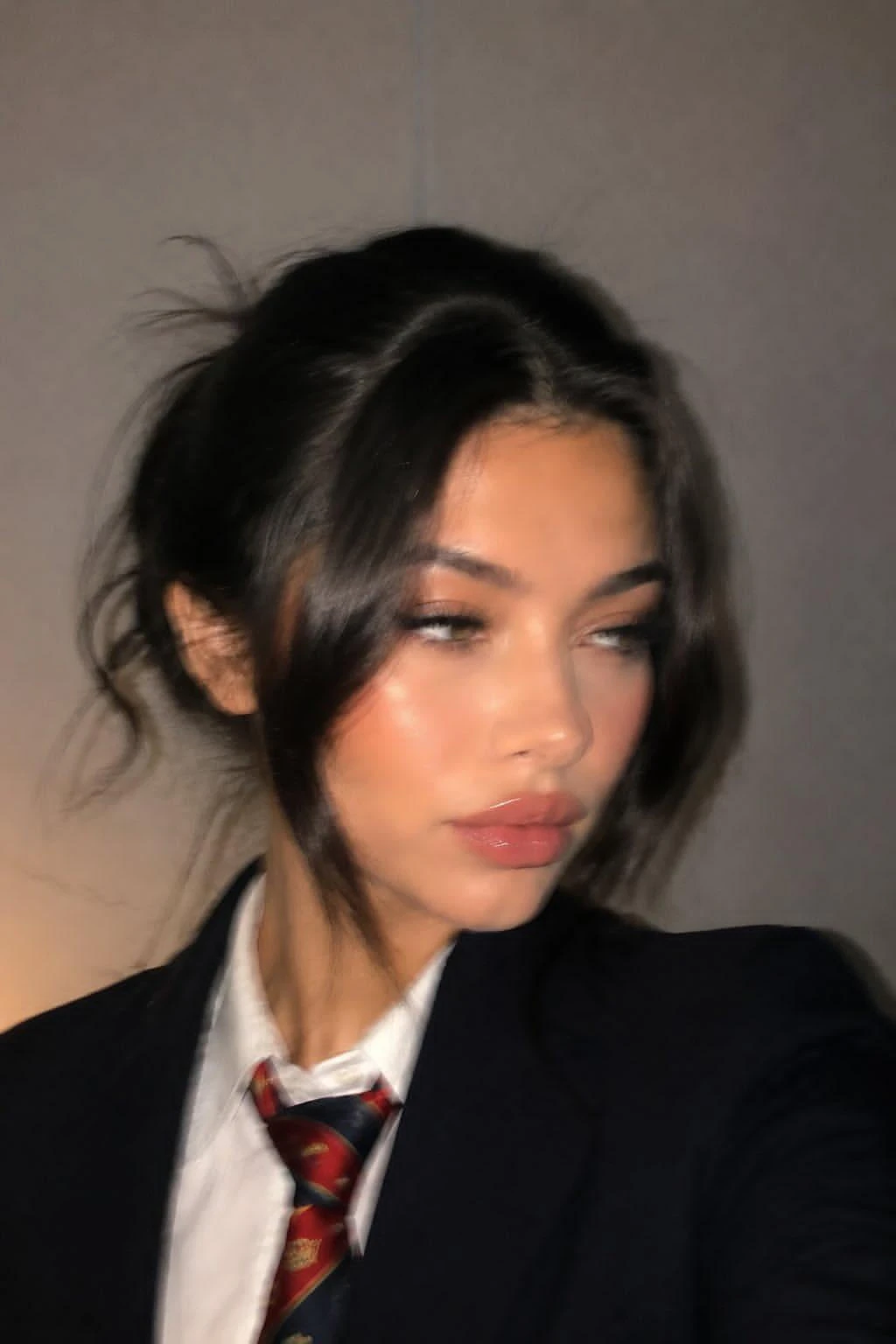 A blurry close-up of a woman with an updo, wearing a blazer and tie, gazing sideways.