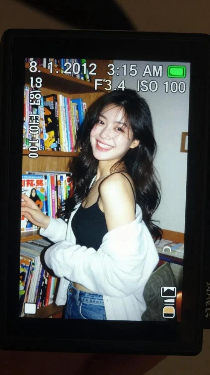 A close-up of a digital camera's LCD screen displays a candid photo of a young woman laughing beside a colorful comic book shelf