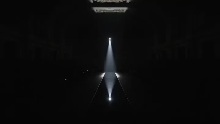 Luxury runway model walks under dramatic Paris fashion show spotlights