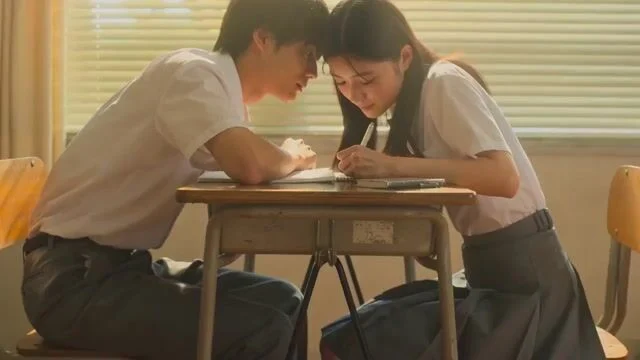 Two Japanese students share a shy glance in a sunlit classroom